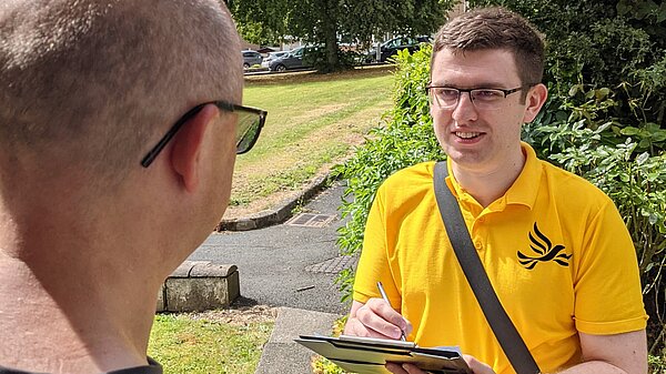 Lib Dem canvasser talking to a resident on the doorstep holding a clipboard and pen