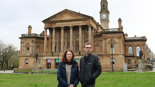 Anne Hannigan and Jack Clark standing next to each other, looking unhappy with Paisley Town Hall in the background.